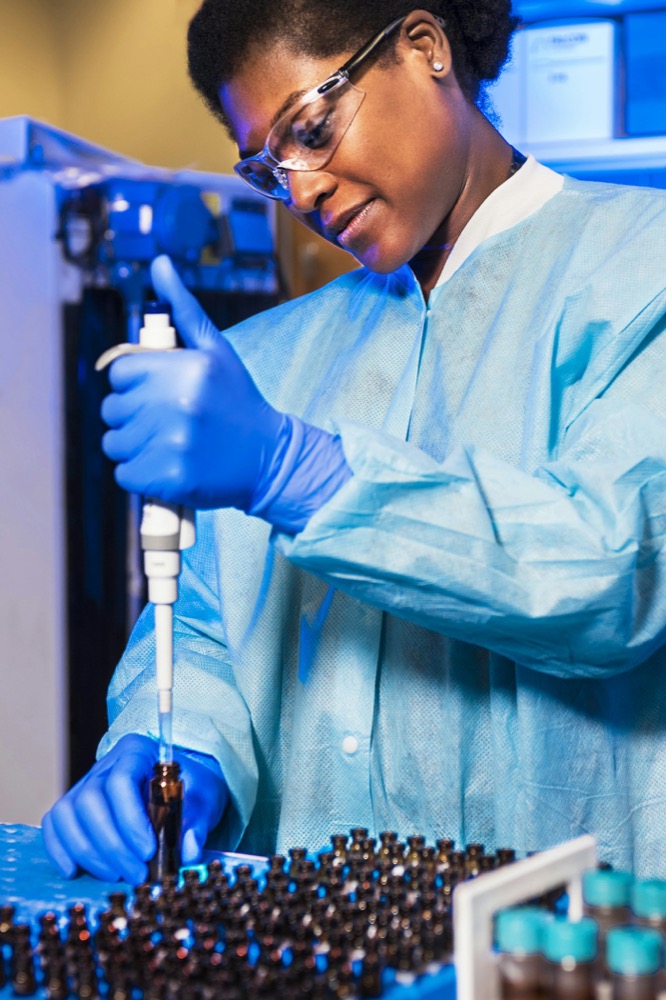 Technicienne en blouse contrôlant des flacons au laboratoire